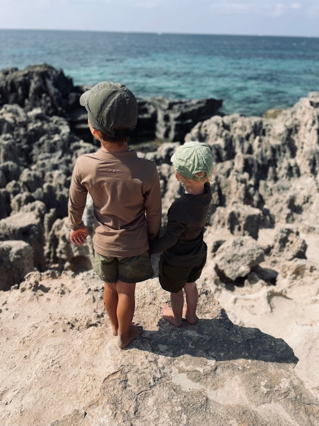 Two children standing on rocky cliffs overlooking the ocean.